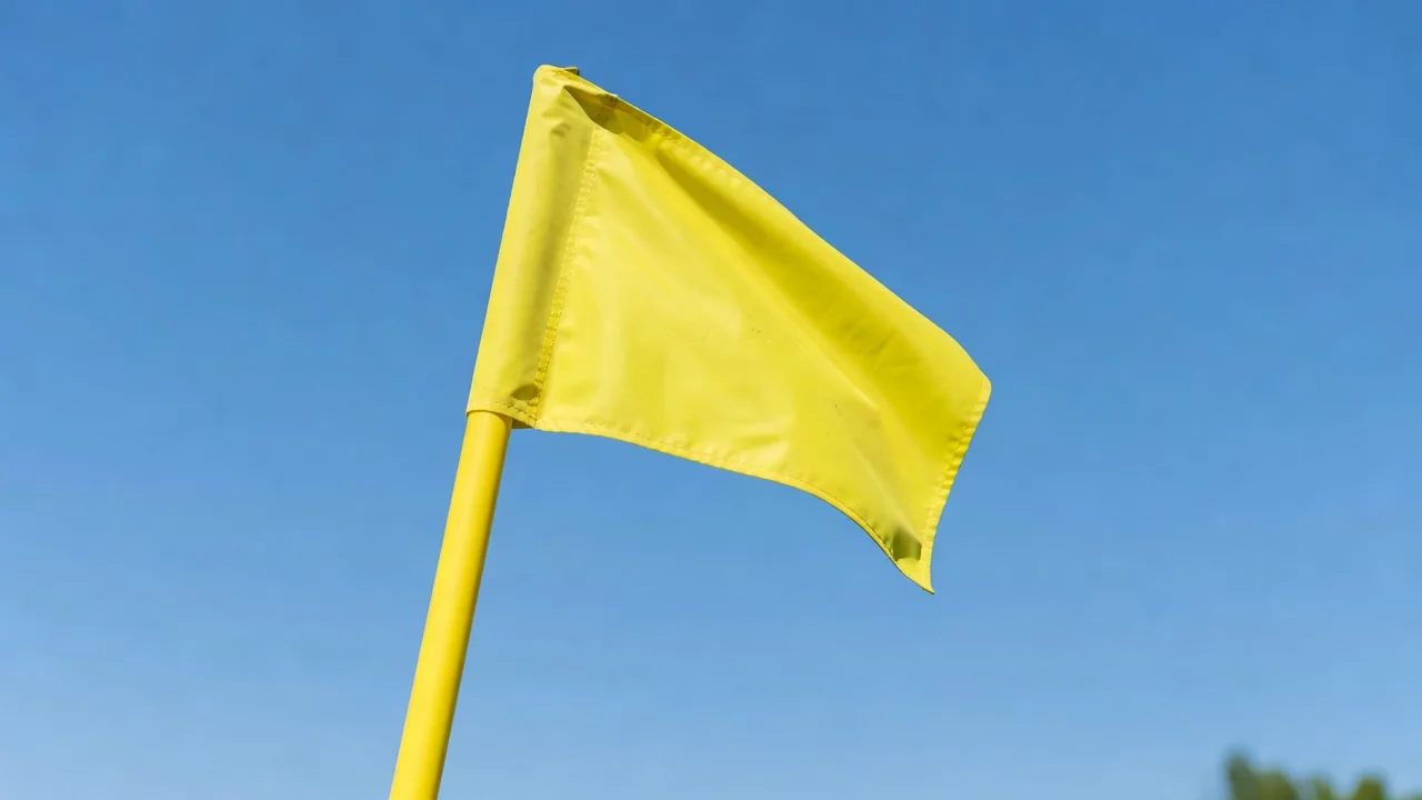 Corner flag in bright yellow against a blue sky above a football pitch